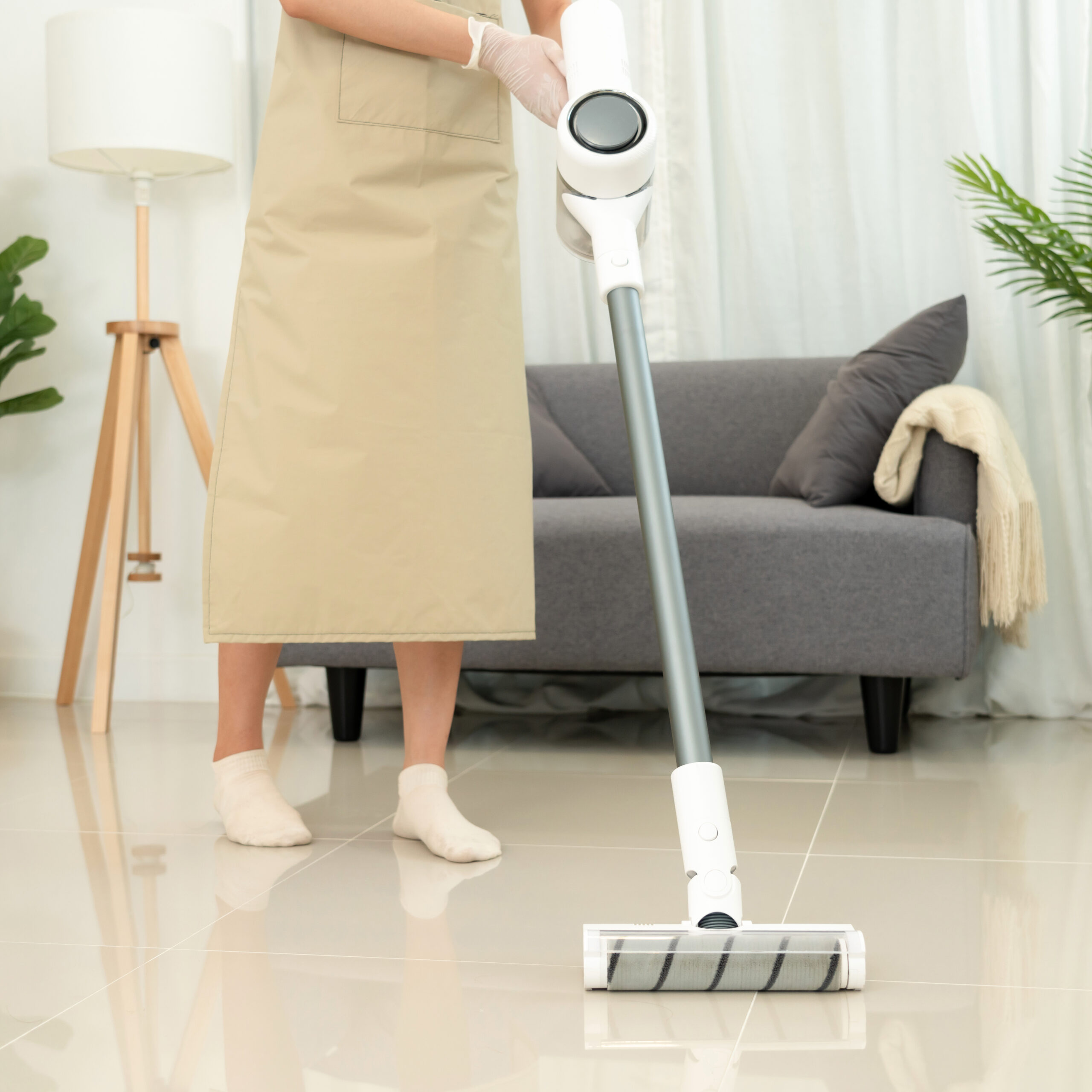 Housekeeper is use mop with vacuum cleaner to housekeeping with vacuuming and wiping dirty laminate on the floor in living room while working to perform routine house cleaning.